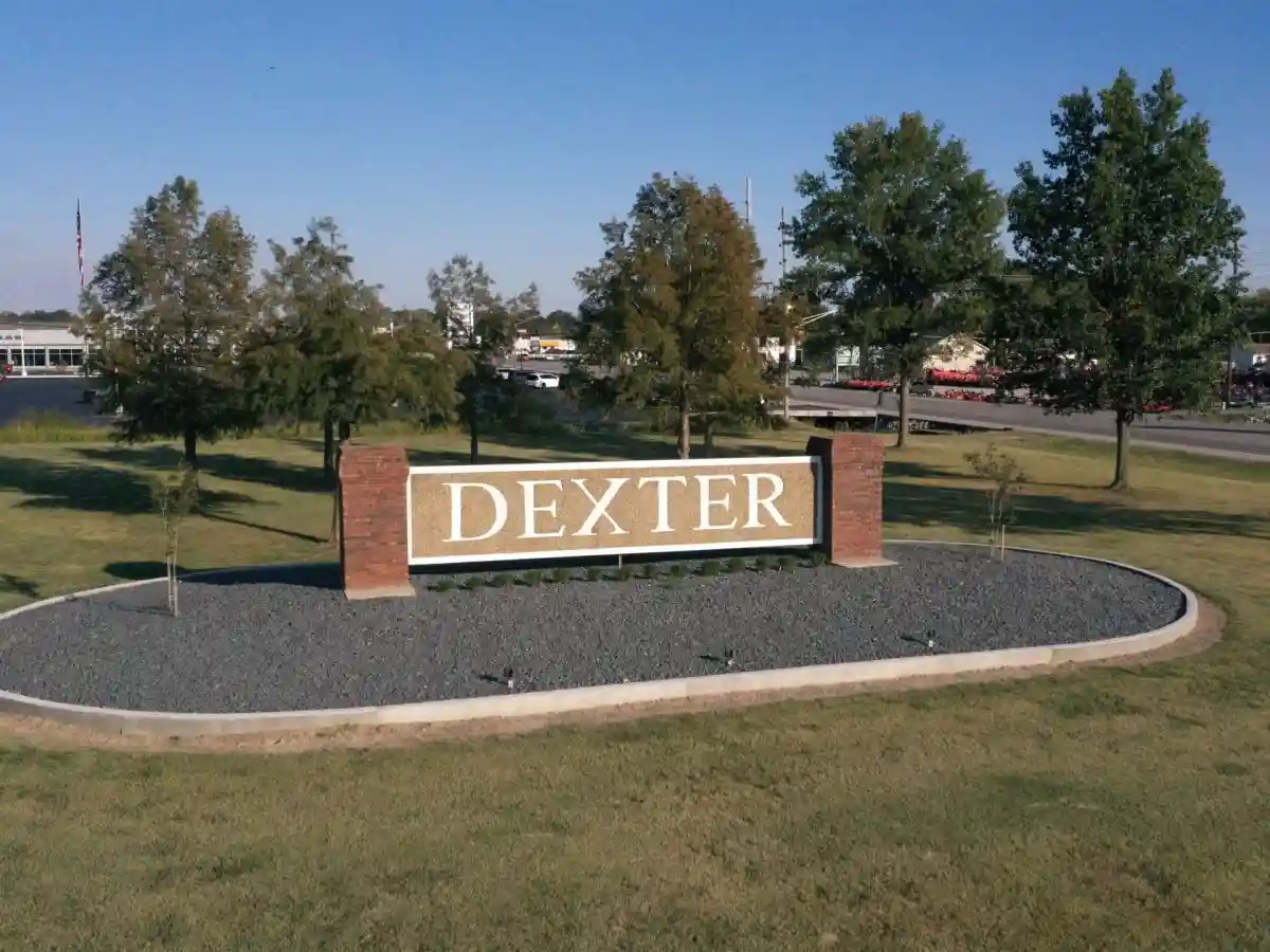 A stone and brick welcome sign reading "Dexter" surrounded by landscaping at the edge of town.